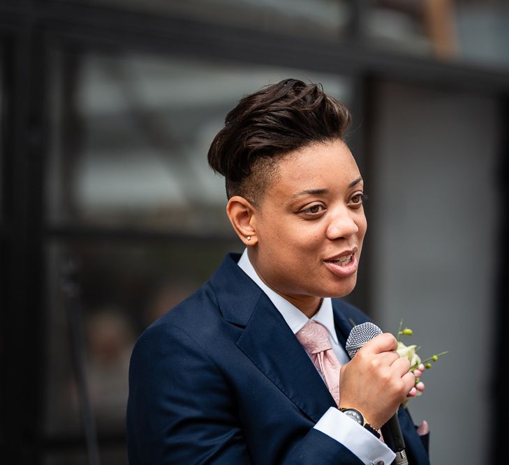 Bride in Navy Wedding Suit with Pink Tie Delivering Her Wedding Speech