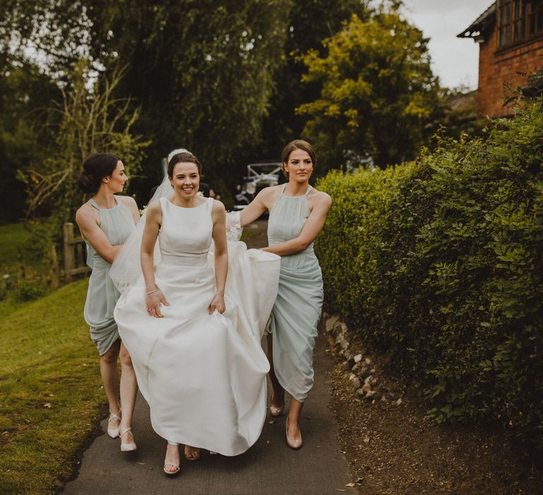 Bridesmaids in pale green dresses holding up the brides Pronovias wedding dress