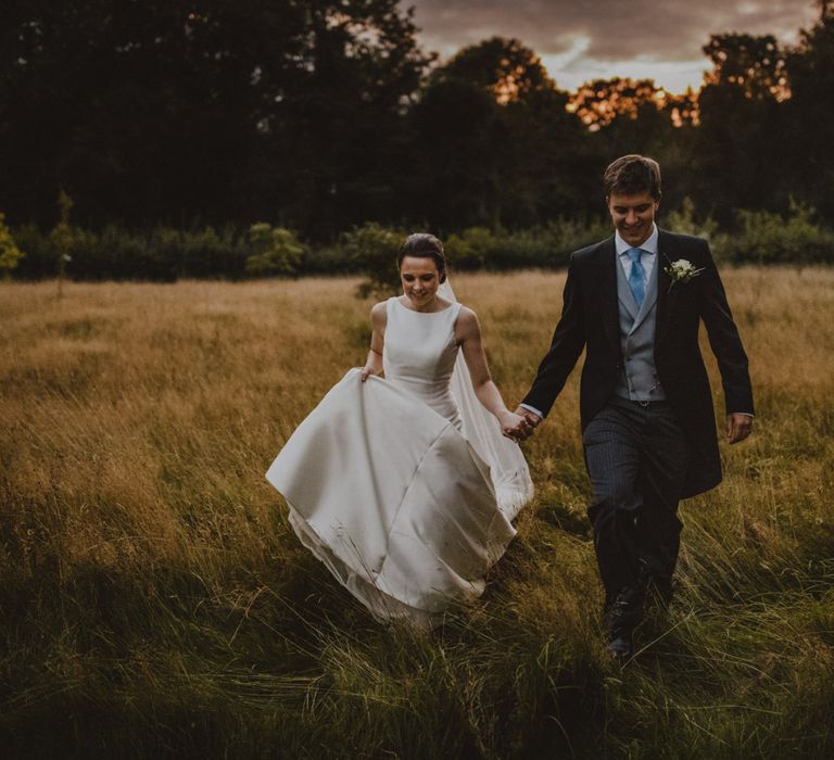 Bride and groom walking through the fields during sunset