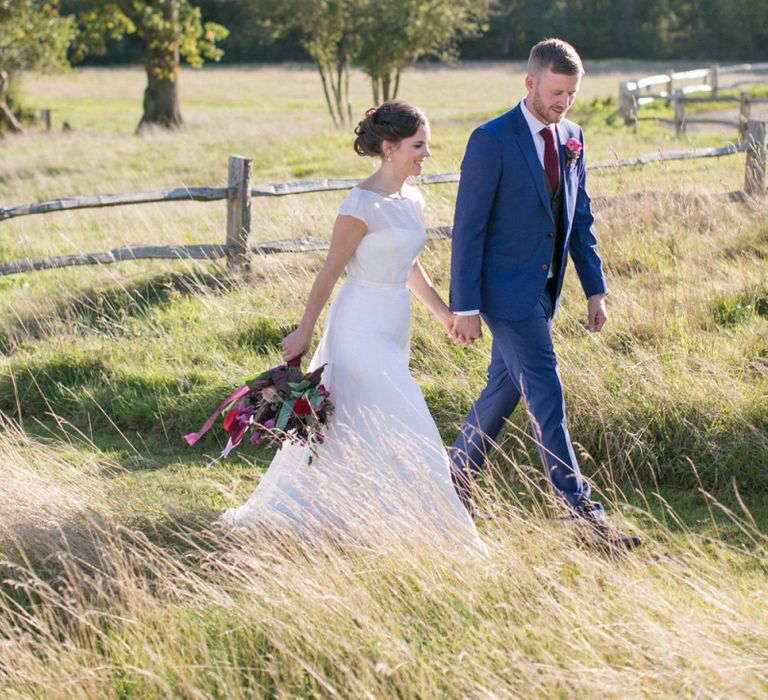 Bride in Jesus Peiro Wedding Dress and Groom in Blue  Hugo Boss Suit Walking Through  the Countryside