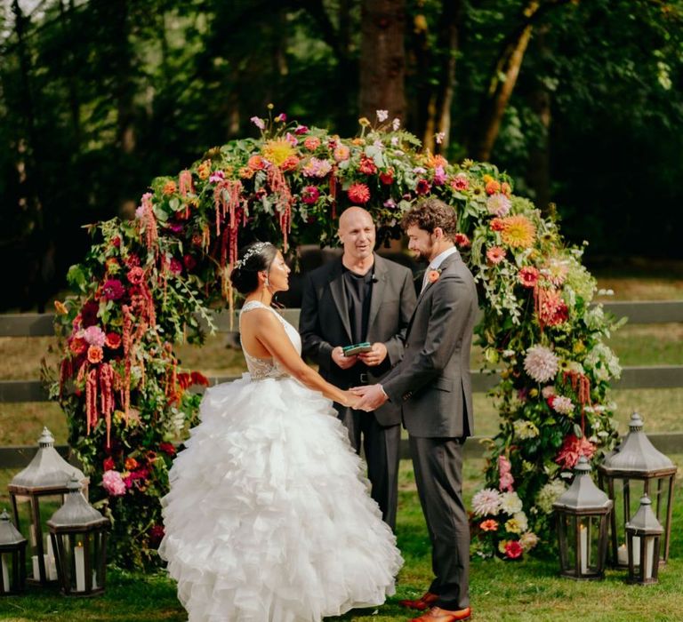 Bride and groom exchanging vows in front of the flower arch