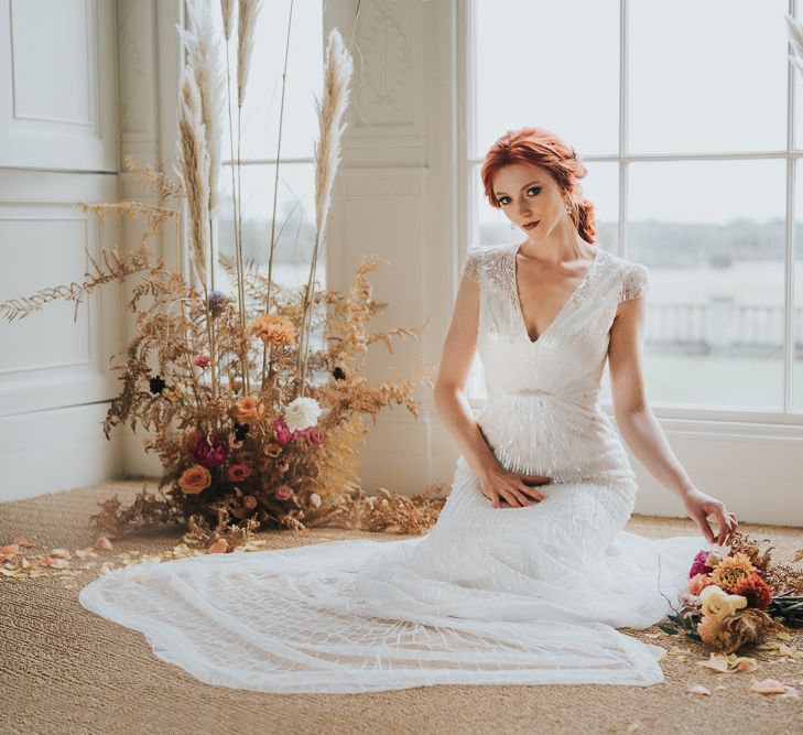 Bride sitting in between dried grasses with pink and orange flower arrangements