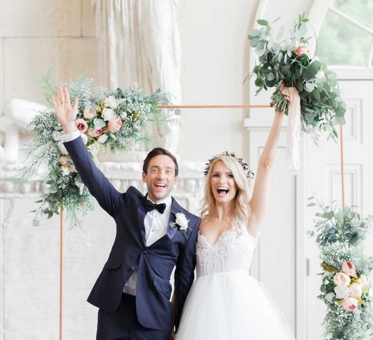 Bride and groom celebrate wedding in front of copper pipe and flower structure