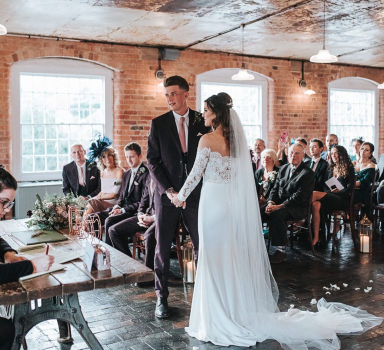 Bride in Lace Bardot Wedding Dress Holding Hands at The Altar with Her Groom in a Moss Bros. Suit