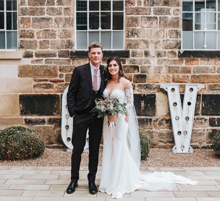 Bride in Pronovias Dracma Bardot Wedding Dress and Groom in Tailor Me Moss Bros. Suit Posing in Front of Giant LOVE Letters