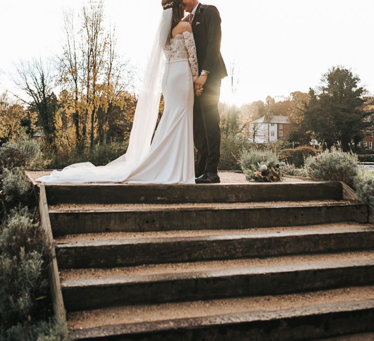 Bride in Pronovias Dracma Bardot Wedding Dress and Groom in Tailor Me Moss Bros. Suit Kissing