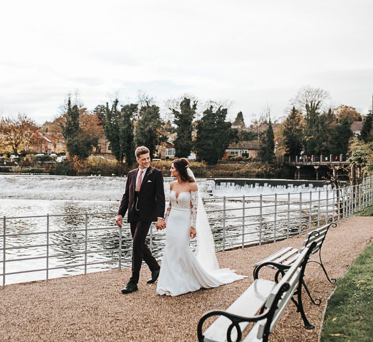 Bride in Lace Bardot Wedding Dress and Groom in Tailor Me Moss Bros. Suit Walking by the River Bank