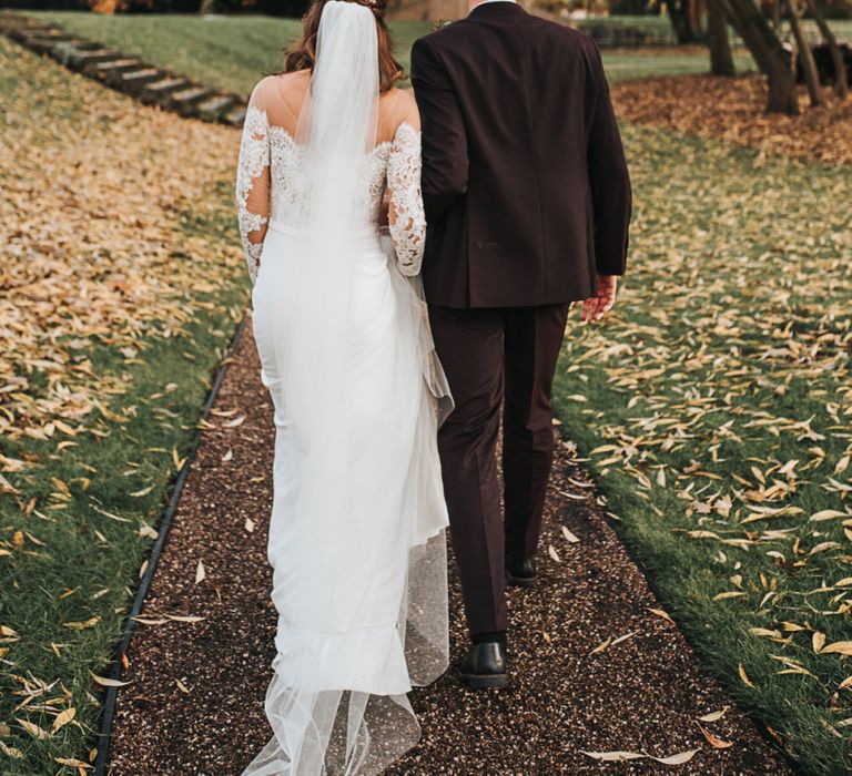 Bride in Lace Bardot Wedding Dress and Groom in Tailor Me Moss Bros. Suit Walking Through the Fallen Leaves