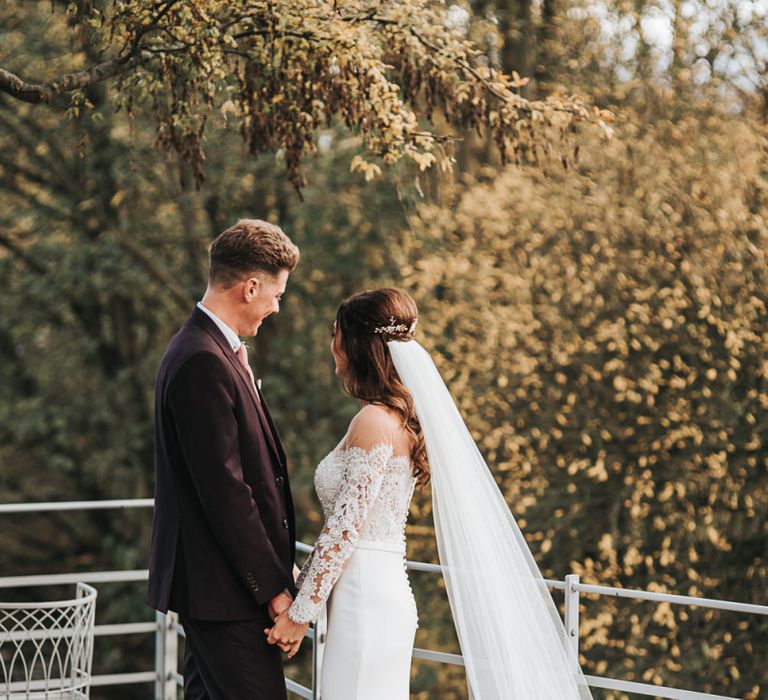 Bride in Pronovias Dracma Bardot Wedding Dress and Groom in Tailor Me Moss Bros. Suit Holding Hands