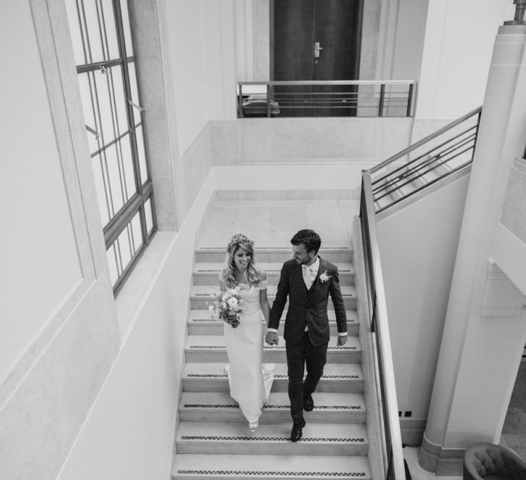 Bride in Lace Off The Shoulder Jennifer Regan Wedding Dress and Flower Crown and Groom in Grey Suit Walking Down Hackney Town Hall Steps