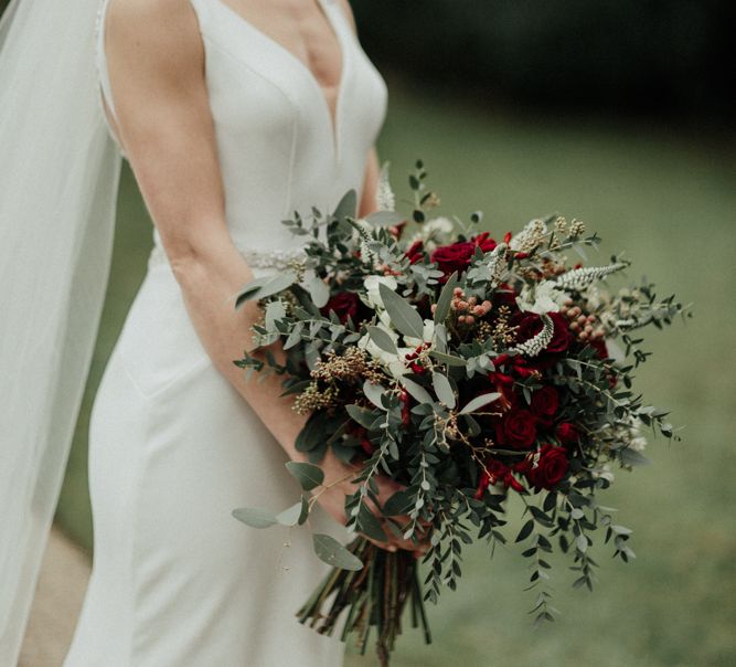 Bride in Essense of Australia Wedding Dress with Straps Holding a Red Flower and Foliage Winter Wedding Bouquet