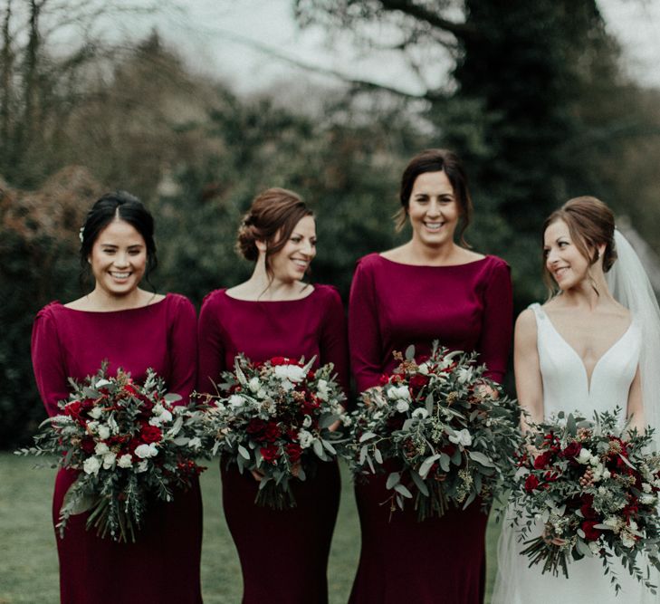 Bridal Party with Bridesmaids in Burgundy Dresses and Bride in Essense of Australia Wedding Dress Holding Red and Foliage Winter Bouquets