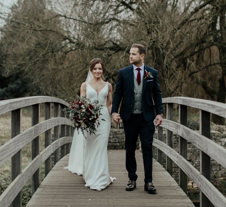 Bride in Essense of Australia Wedding Dress and Cathedral Veil and Groom in Marks and Spencer Suit Walking on a Bridge at Cripps Barn