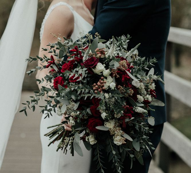 Green and Red Winter Wedding Bouquet with Bride in Essense of Australia Wedding Dress and Cathedral Veil and Groom in Marks and Spencer Suit