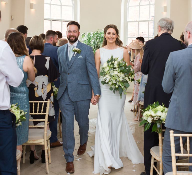 Bride in Pronovias Wedding Dress and Groom in Grey Suit Walking Up The Aisle as Husband and Wife