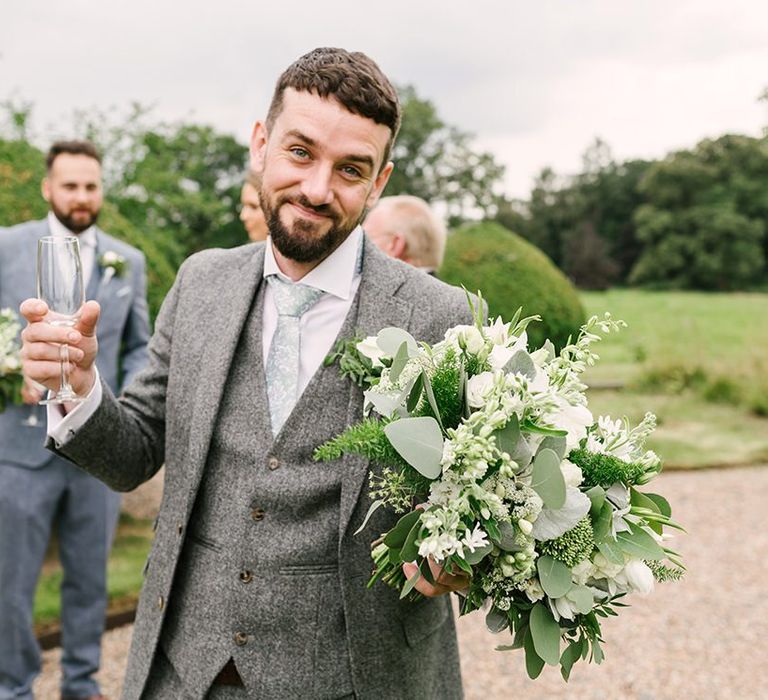 Groomsman in Grey Wedding Suit Holding a White and Green Wedding Bouquet