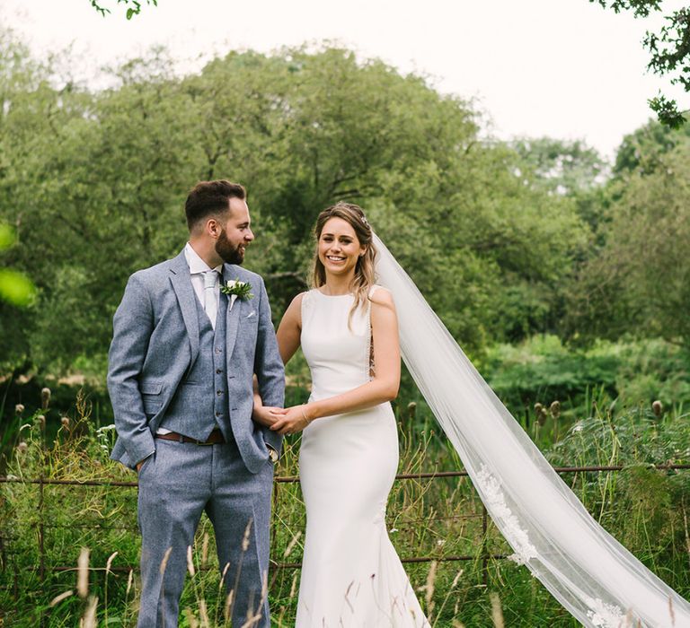 Bride in Fitted Pronovias Wedding Dress Holding Her Grooms Arm  in a Light Grey Wedding Suit