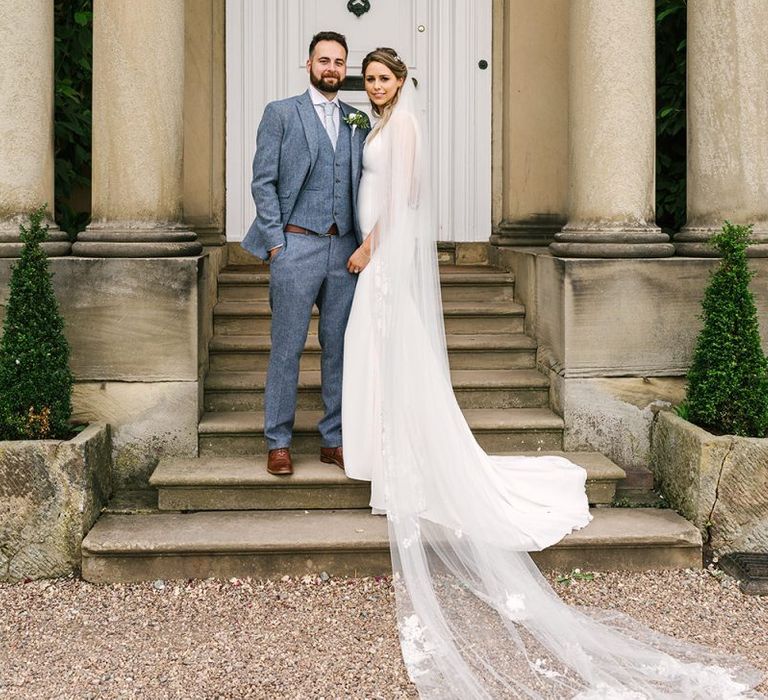 Bride in Pronovias Wedding Dress and Cathedral Length Veil and Groom in Grey Wedding Suit