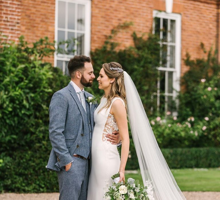 Bride in Pronovias Wedding Dress with Lace Side Inserts and Groom in Light Grey Wedding Suit