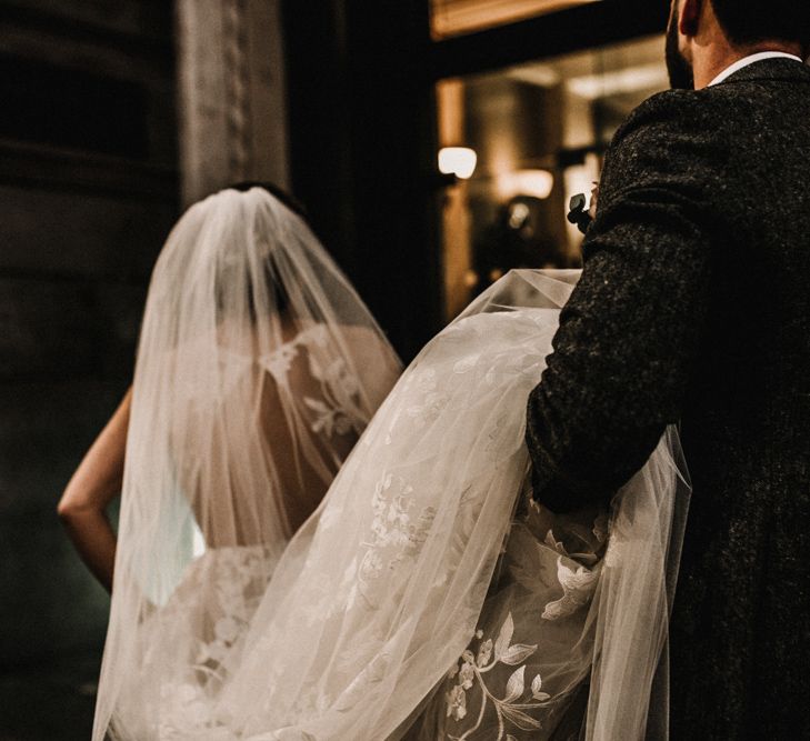 Groom in Wool Walker Slater Three-piece Suit Holding Up His Brides in Hayley Paige Wedding Dress Train and Veil