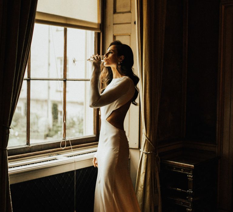 Beautiful Bride Standing at The Window  Sipping Champagne