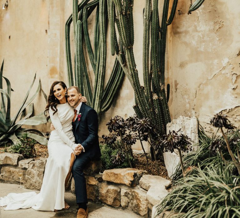 Bride Sitting on Her Grooms Knee with Tropical Plants Backdrop