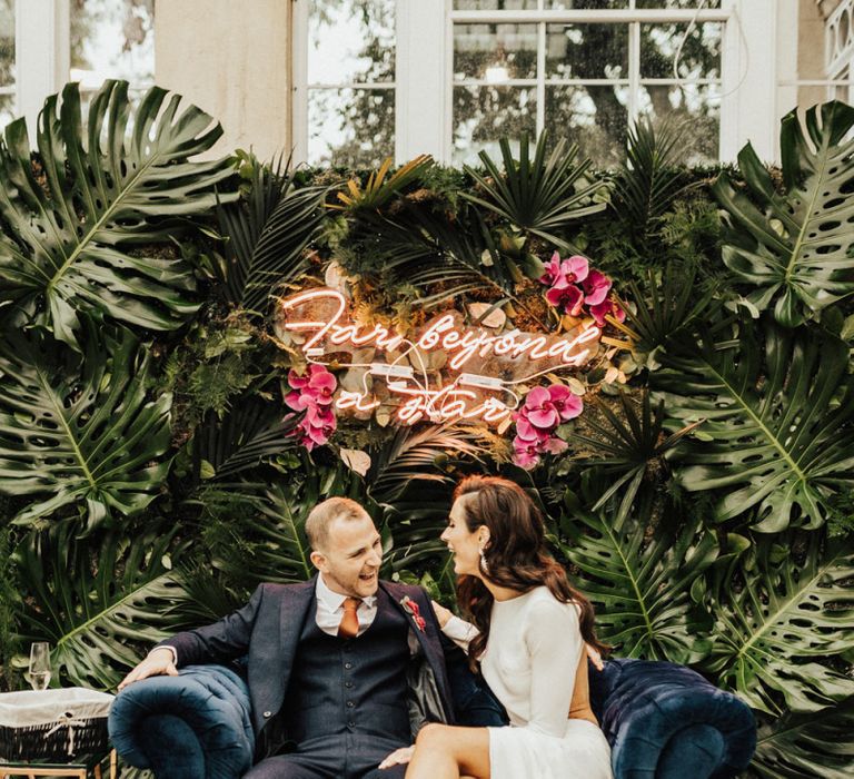 Bride and Groom Sitting on a Love Seat with Neon Sign Wedding Sign