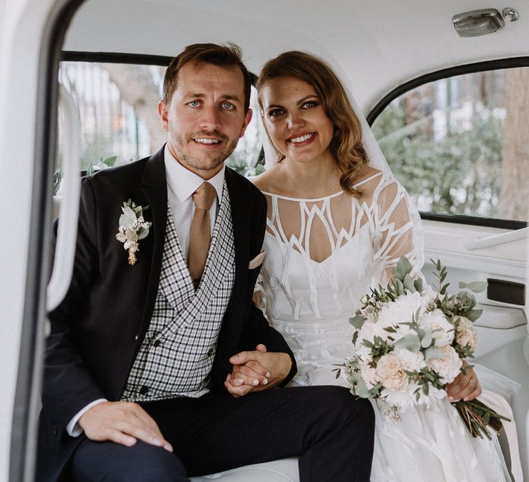 Bride in Embroidered Tulle Halfpenny London Dress with High Neckline, Batwing Sleeves and Low V-Back | Fingertip Length Veil from Florence &amp; Dot | Bridal Bouquet of White and Blush Pink Flowers with Eucalyptus and Trailing Silk Ribbon | Groom in Navy Slim Fit Suit with Checked Double Breasted Waistcoat and Blush Pink Knitted Tie | Wedding Ceremony at Stoke Newington Town Hall | Floral Arch and Bride in Batwing Sleeve Halfpenny Dress for London Pub Wedding | Caitlin + Jones