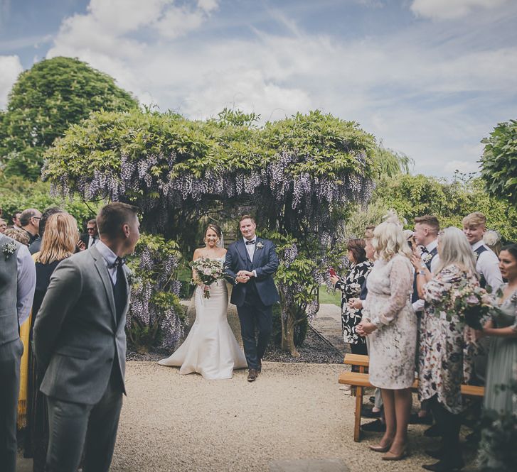 Bride in flat wedding shoes walks up to outdoor ceremony