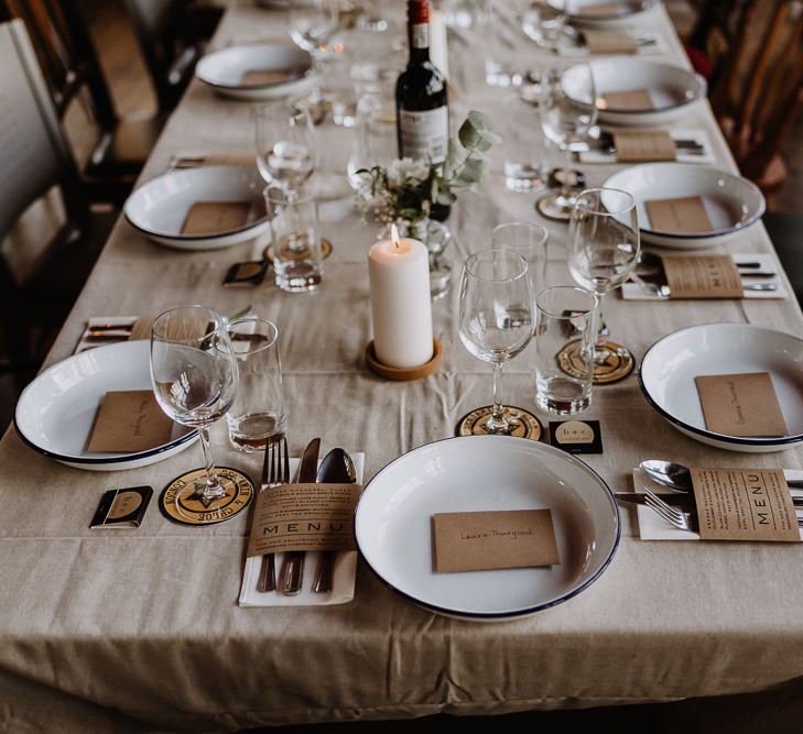 Kraft Paper Wedding Breakfast Menus | White Enamel Plates with Blue Rim | White Pillar Candle | Bud Vase with White Flowers and Eucalyptus | Banquet Table | Mismatched Chairs | Floral Arch and Bride in Batwing Sleeve Halfpenny Dress for London Pub Wedding | Caitlin + Jones