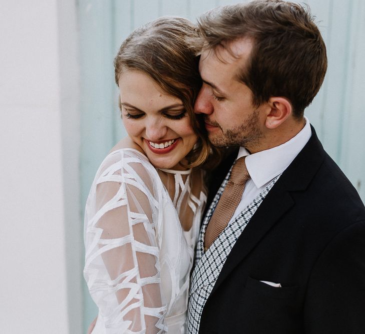 Bride in Embroidered Tulle Halfpenny London Dress with High Neckline, Batwing Sleeves and Low V-Back | Groom in Navy Slim Fit Suit with Checked Double Breasted Waistcoat and Blush Pink Knitted Tie | Floral Arch and Bride in Batwing Sleeve Halfpenny Dress for London Pub Wedding | Caitlin + Jones