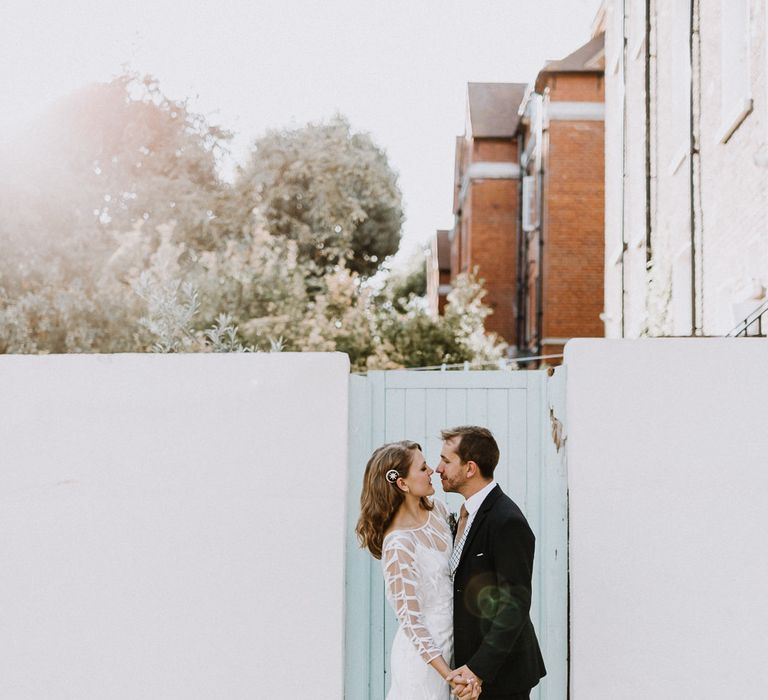 Bride in Embroidered Tulle Halfpenny London Dress with High Neckline, Batwing Sleeves and Low V-Back | Anthropologie Hairpiece | Groom in Navy Slim Fit Suit with Checked Double Breasted Waistcoat and Blush Pink Knitted Tie | Floral Arch and Bride in Batwing Sleeve Halfpenny Dress for London Pub Wedding | Caitlin + Jones