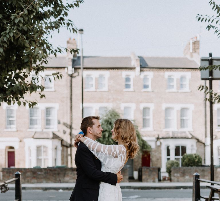 Bride in Embroidered Tulle Halfpenny London Dress with High Neckline, Batwing Sleeves and Low V-Back | Groom in Navy Slim Fit Suit with Checked Double Breasted Waistcoat and Blush Pink Knitted Tie | Floral Arch and Bride in Batwing Sleeve Halfpenny Dress for London Pub Wedding | Caitlin + Jones