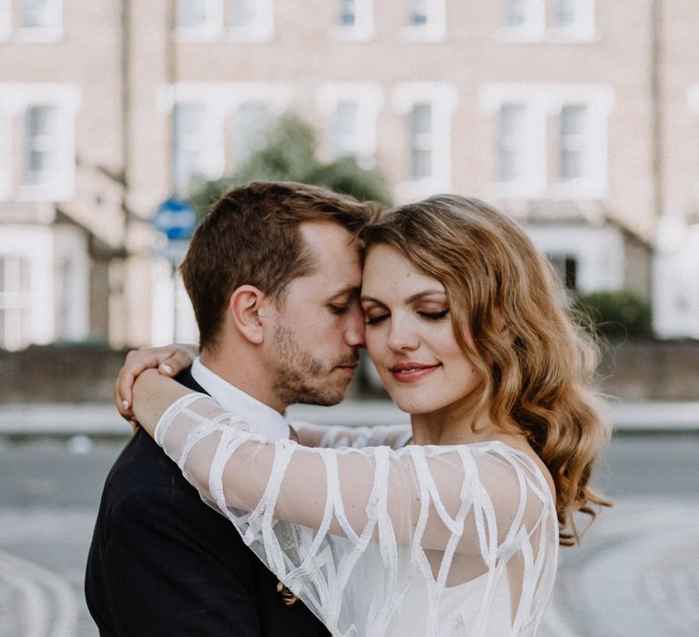 Bride in Embroidered Tulle Halfpenny London Dress with High Neckline, Batwing Sleeves and Low V-Back | Groom in Navy Slim Fit Suit with Checked Double Breasted Waistcoat and Blush Pink Knitted Tie | Floral Arch and Bride in Batwing Sleeve Halfpenny Dress for London Pub Wedding | Caitlin + Jones