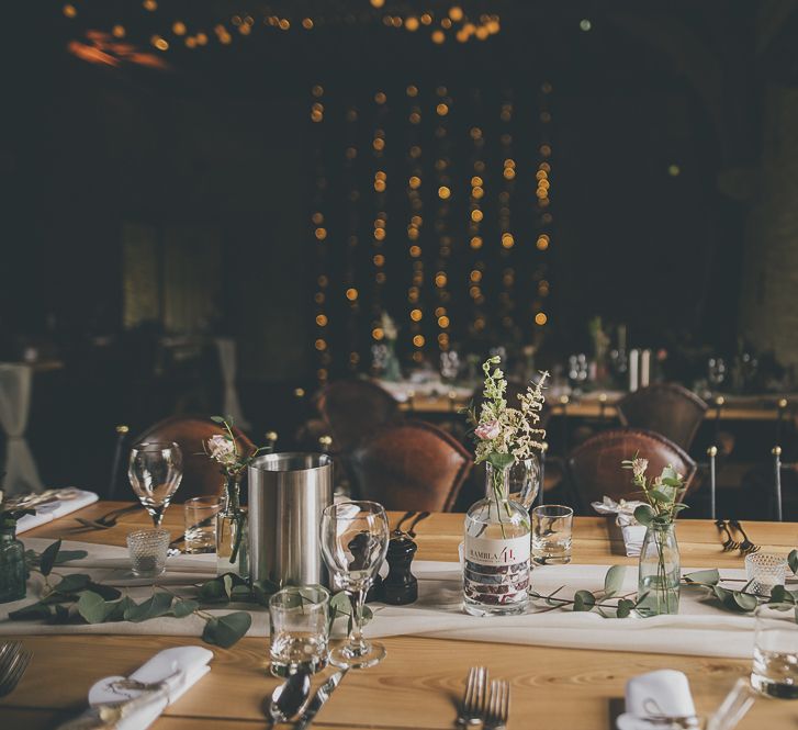 Single stem flowers in glass bottles for table decor at rustic wedding