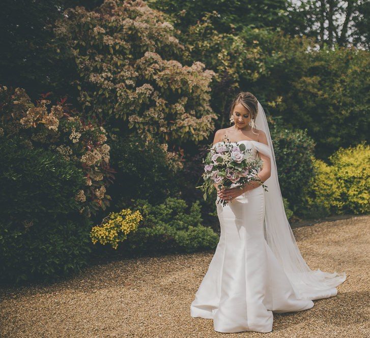 Bride in flat wedding shoes in off-the-shoulder mermaid wedding dress and lilac bouquet