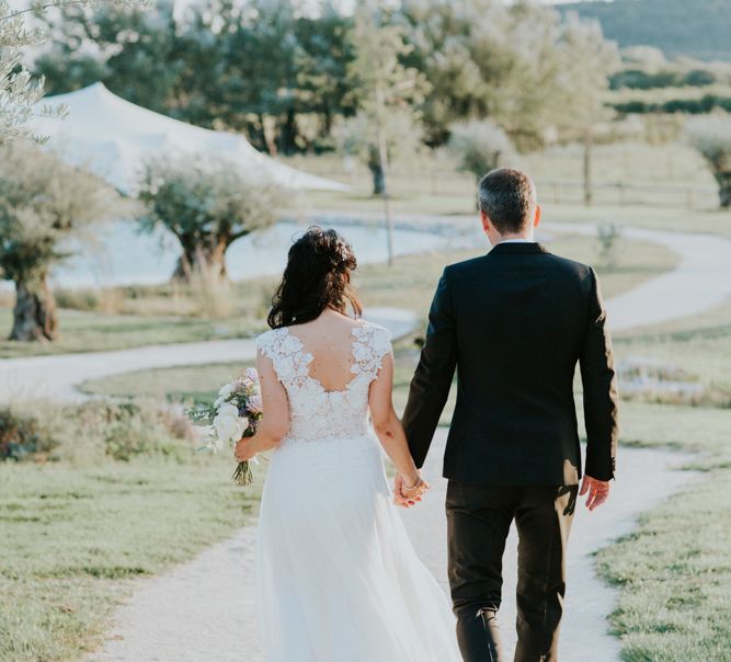 Bride in Appliqué Caroline Castigliano Wedding Dress and Groom in Tuxedo Walking Down a Country Lane