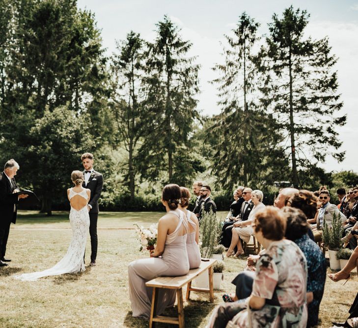 Wedding Vows | Wedding Arch Sculpted from Trees | Aisle Lined with Potted Shrubbery and Trees | Bride in Embroidered Grace Loves Lace Gown with Fringing and Cut Out Back | Groom in Black Gagliardi Suit with Bow Tie and Braces | Bridesmaids in Halterneck Dusty Pink TFNC Dresses | Bridesmaids Bouquets of Mixed Flowers and Foliage with Burnt Orange Trailing Ribbon | Outdoor Ceremony at Fishley Hall with Grace Loves Lace Fringe Dress | Darina Stoda Photography