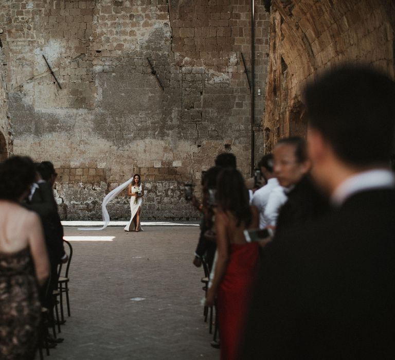 Entrance of the Bride | Bride in Silk Pallas Couture Wedding Dress with Plunging Neckline and Side Split | Roman &amp; French Cathedral Veil | Long Stemmed Bridal Bouquet of White Flowers | Salvatore Ferragamo Nude Bridal Shoes | Intimate Italian Castle Wedding with Prosecco Tower | James Frost Photography