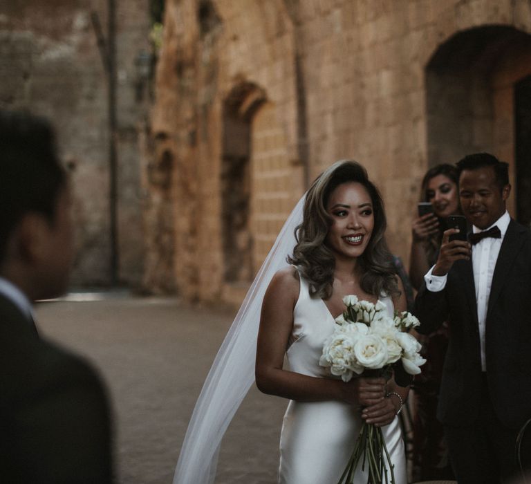 Entrance of the Bride | Bride in Silk Pallas Couture Wedding Dress with Plunging Neckline and Side Split | Roman &amp; French Cathedral Veil | Long Stemmed Bridal Bouquet of White Flowers | Intimate Italian Castle Wedding with Prosecco Tower | James Frost Photography