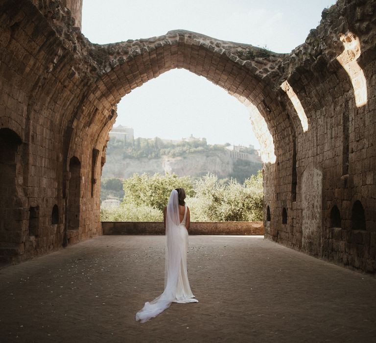 Bride in Silk Pallas Couture Wedding Dress with Plunging Neckline and Side Split | Roman &amp; French Cathedral Veil | Intimate Italian Castle Wedding with Prosecco Tower | James Frost Photography