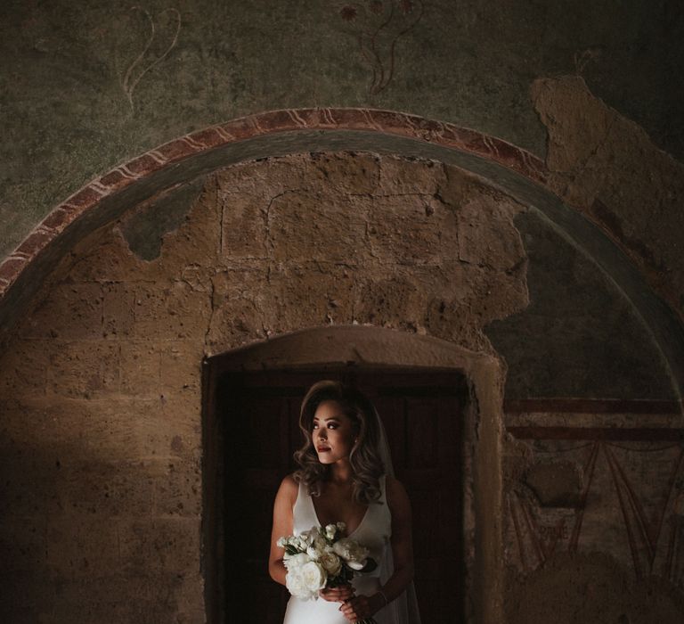 Bride in Silk Pallas Couture Wedding Dress with Plunging Neckline and Side Split | Roman &amp; French Cathedral Veil | Long Stemmed Bridal Bouquet of White Flowers | Intimate Italian Castle Wedding with Prosecco Tower | James Frost Photography