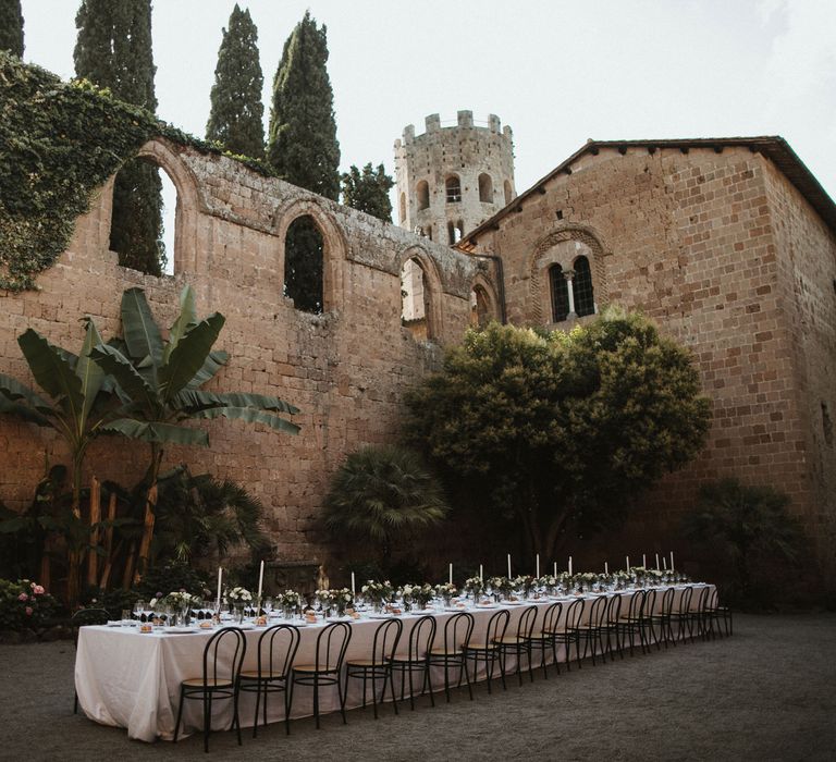 Wedding Breakfast Table in Courtyard at La Badia Di Orvieto Italy | White Tapered Candles | Hurricane Vases with White Flowers and Foliage | Intimate Italian Castle Wedding with Prosecco Tower | James Frost Photography