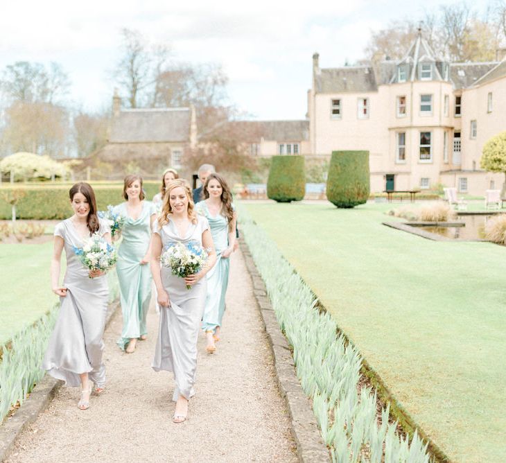 Bridesmaids in Grey and Green Ghost Satin Dresses  Walking Through the Wedding Venue Gardens