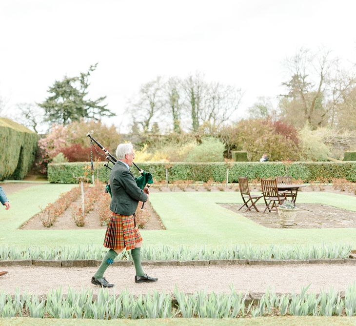 Bride and Groom Walking through the Wedding Venue Gardens Lead by a Bag Piper