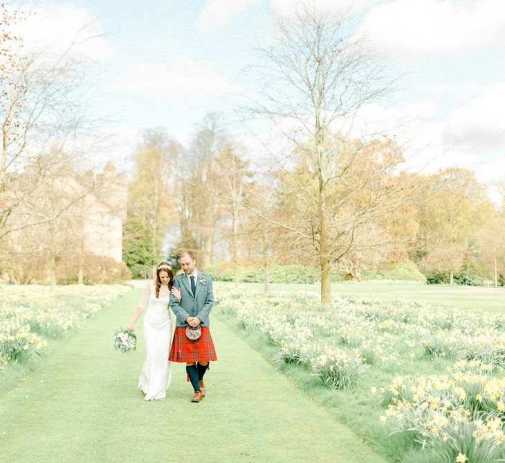 Bride and Groom Walking Through the Wedding Venue Gardens with Daffodil Patches Either Side