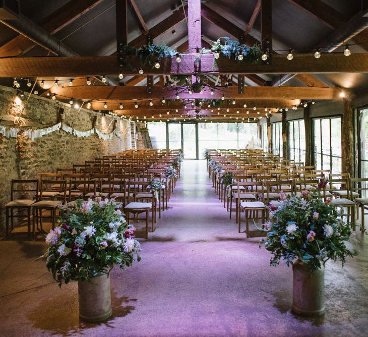 Barn Wedding Ceremony Venue with Two Milk Churns at the Altar Filled with Flowers