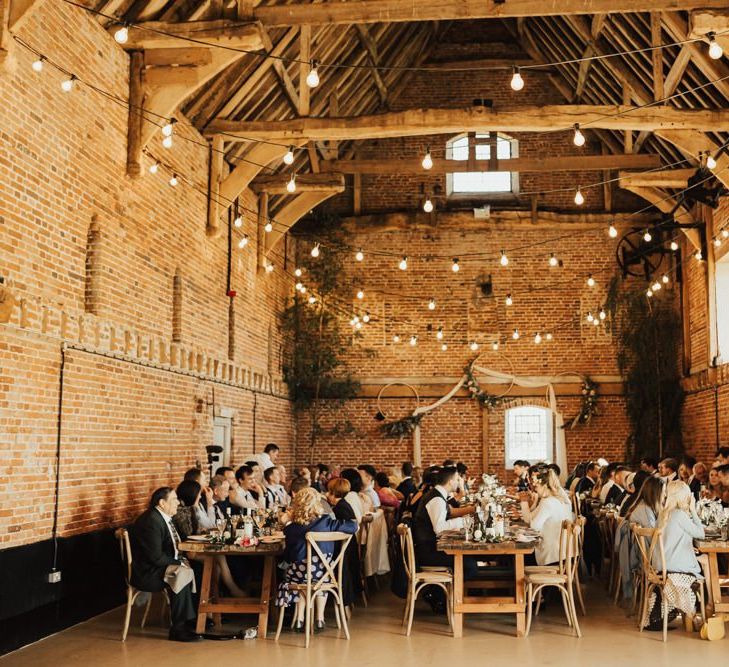 Godwick Barn Wedding Reception with Wooden Tables, Festoon Lights and Foliage Decor