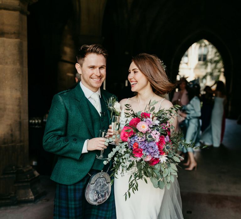 Bride and groom portrait with groom in tartan kilt and bride holding a colourful wedding bouquet