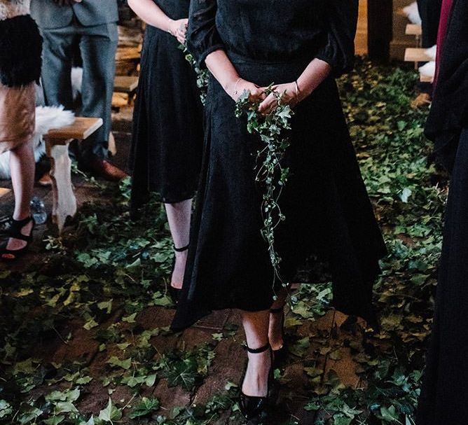 Bridesmaids wearing black laced dresses with foliage decor and bouquets